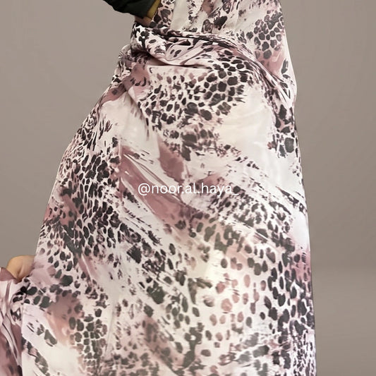 A close-up of a draped fabric or scarf featuring an abstract leopard print pattern in black, gray, and dusty pink on a white base, with a watermark '@nooral.haya' across the center.