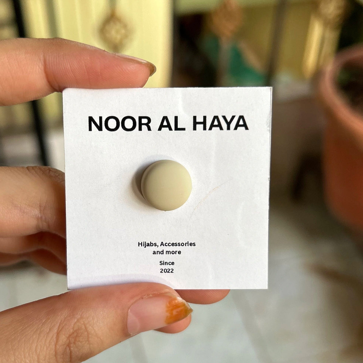 Woman holding a beige hijab magnet by Noor Al Haya on branded card