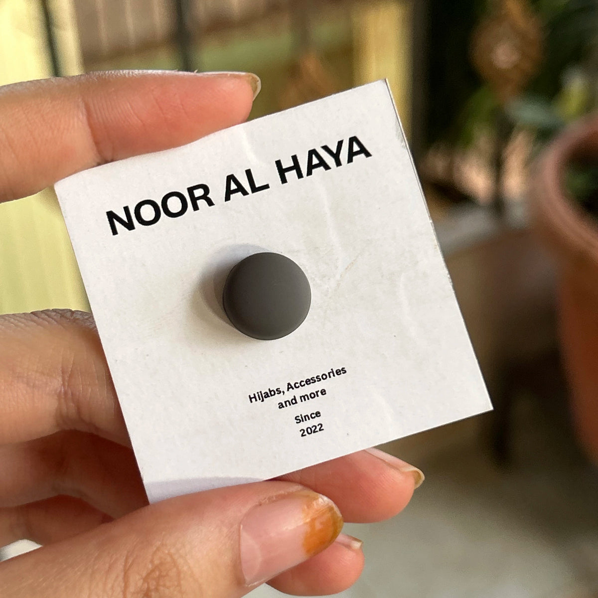 Woman holding dark grey hijab magnet by Noor Al Haya