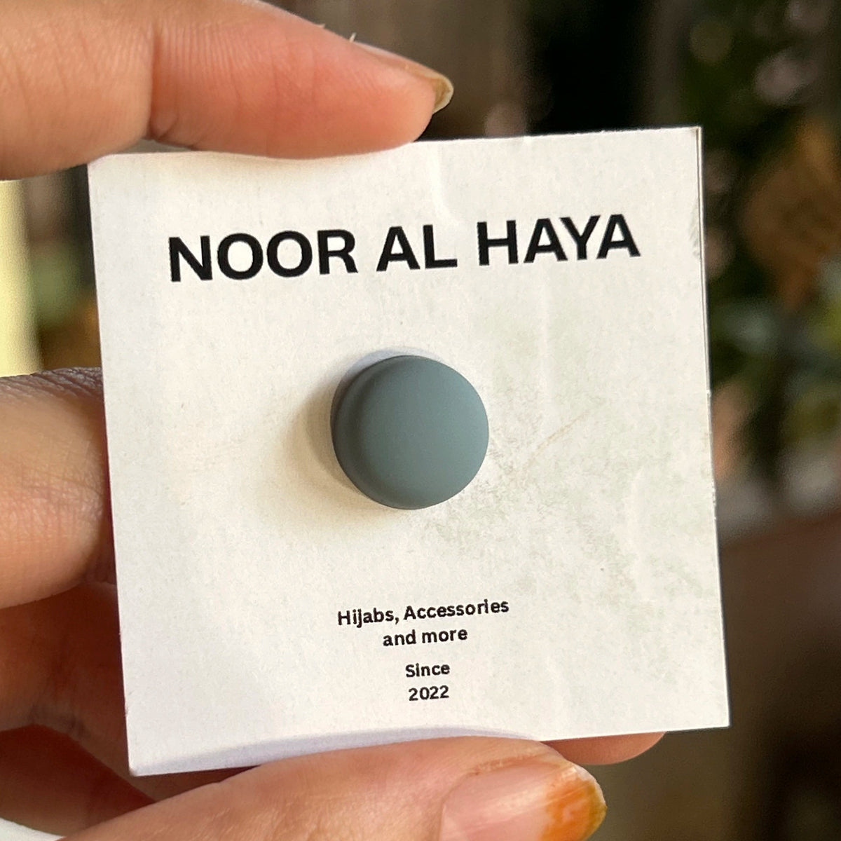 Woman holding grey hijab magnet by Noor Al Haya