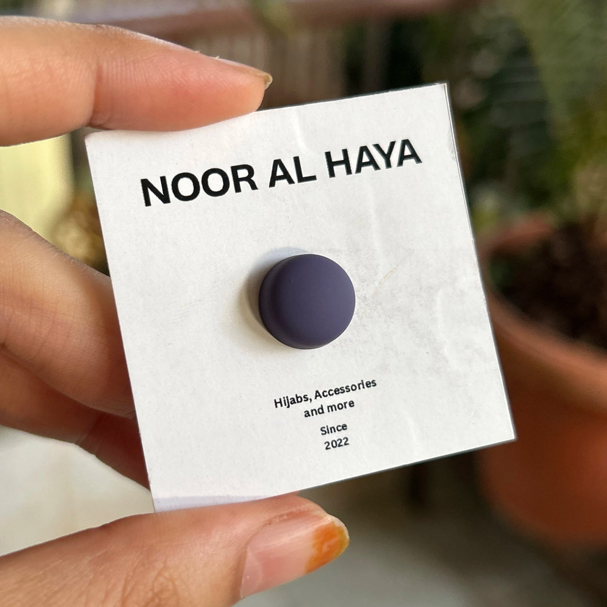 Woman holding a purple hijab magnet by Noor Al Haya on branded card
