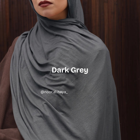 A close-up of a women wearing a draped dark grey luxe jersey hijab by noor al haya