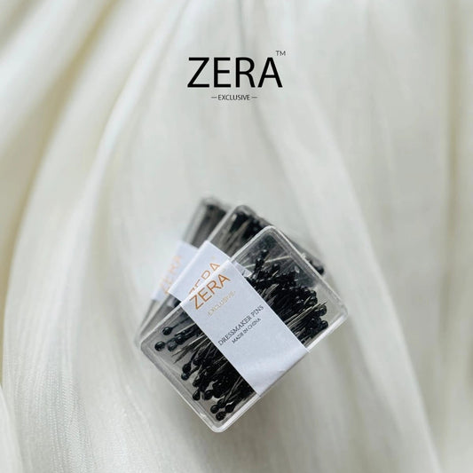 A small clear plastic package of ZERA Hijab Needle Ball Pin Mini in black, displayed on a draped white fabric background with brand text above and product text below.