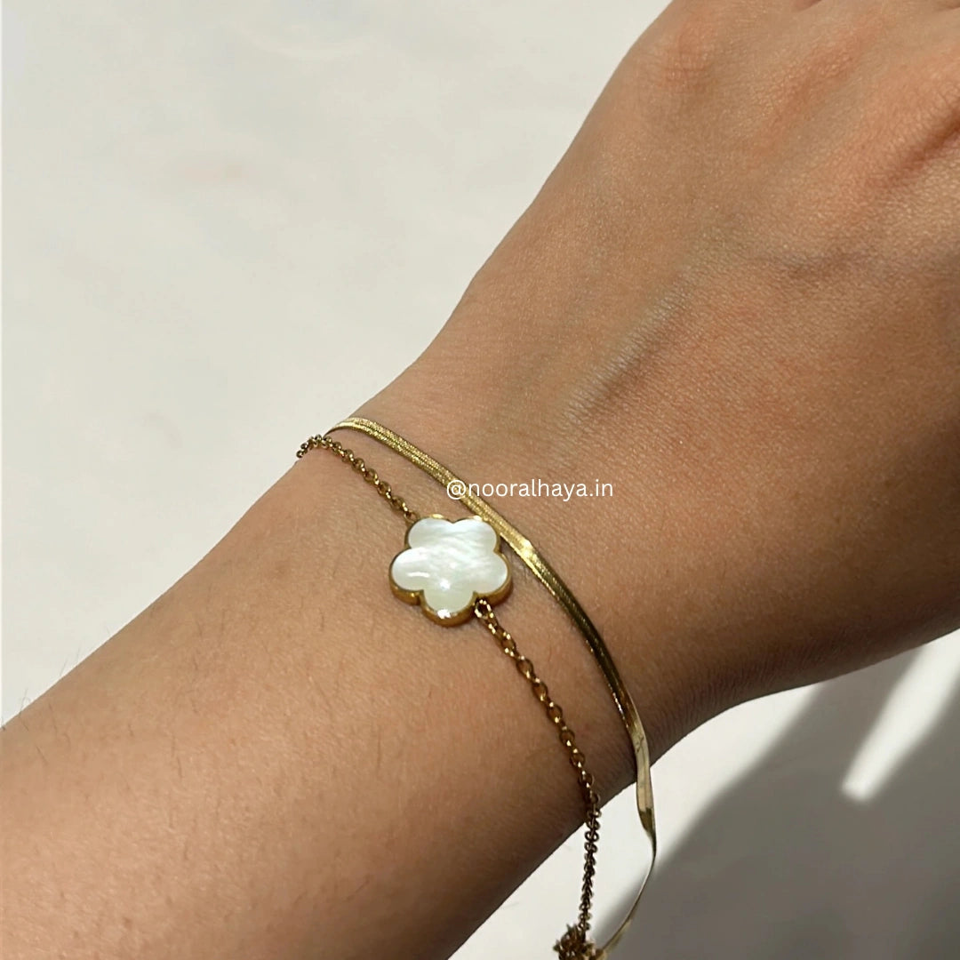 Woman wearing a white clover bracelet with golden chain by Noor Al Haya