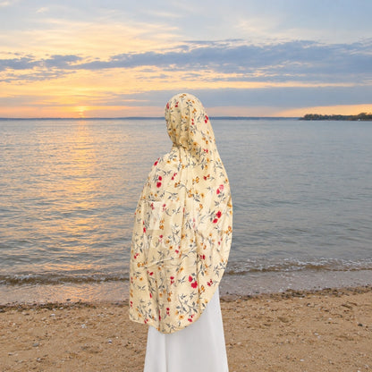 a model wearing yellow floral printed hijab by noor al haya  and standing near shore of sea and watching sunset 